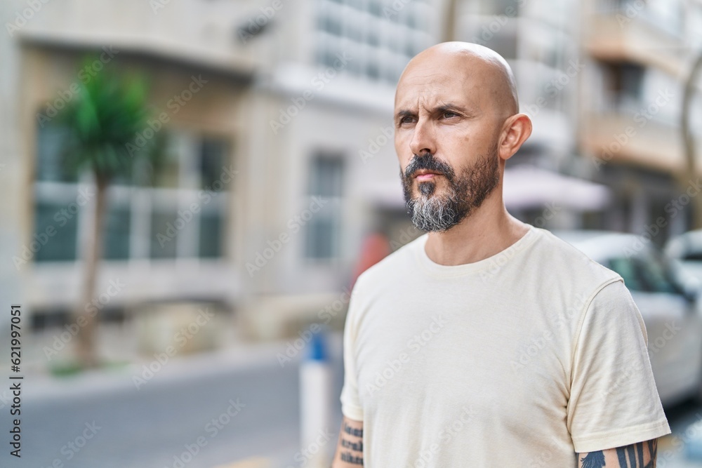 Young bald man looking to the side with serious expression at street Young bald man looking to the side with serious expression at street
