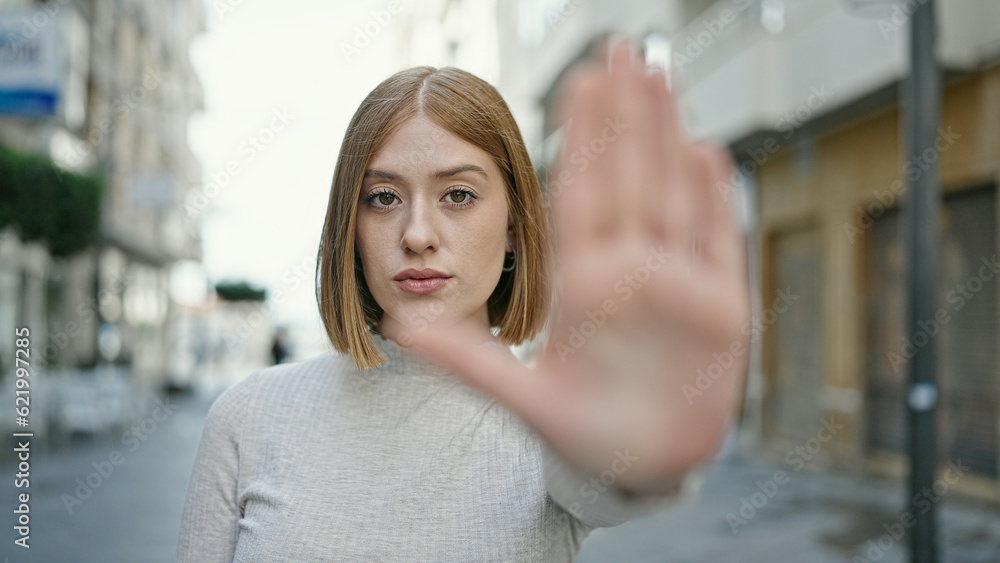 Young blonde woman doing stop gesture with hand at street