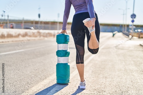 Young beautiful hispanic woman wearing sportswear stretching leg at street