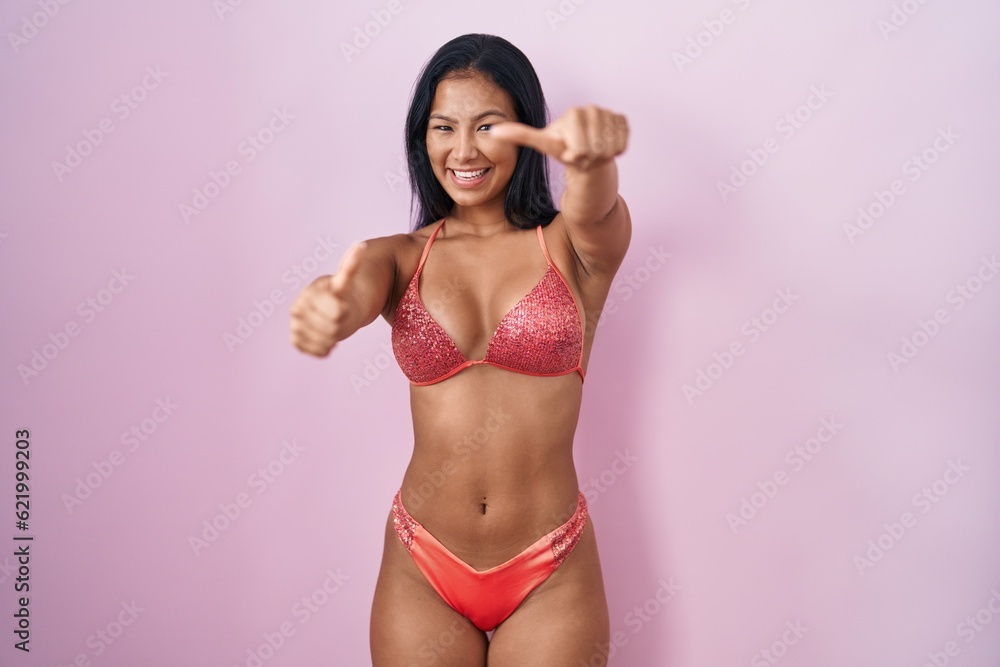 Hispanic woman wearing bikini approving doing positive gesture with hand, thumbs up smiling and happy for success. winner gesture. Hispanic woman wearing bikini approving doing positive gesture with hand, thumbs up smiling and happy for success. winner gesture.