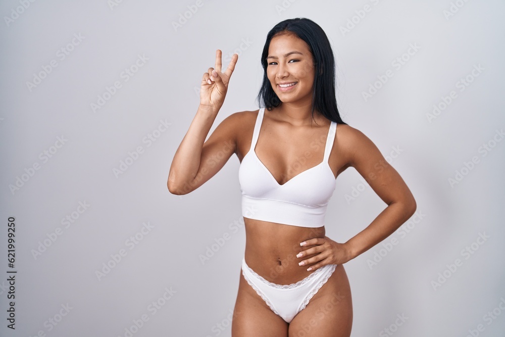 Hispanic woman wearing lingerie smiling looking to the camera showing fingers doing victory sign. number two. Hispanic woman wearing lingerie smiling looking to the camera showing fingers doing victory sign. number two.