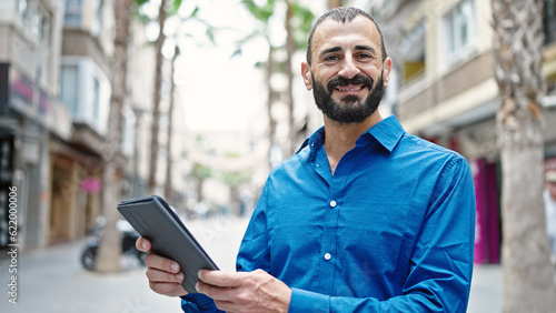 Young hispanic man smiling confident using touchpad at street