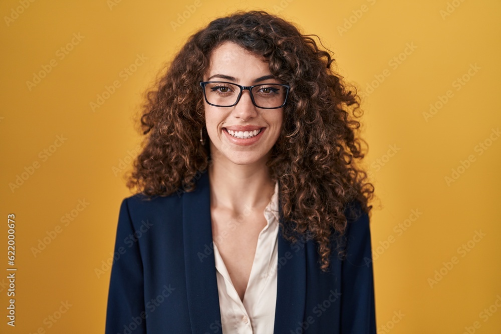 Hispanic woman with curly hair standing over yellow background with a happy and cool smile on face. lucky person.
