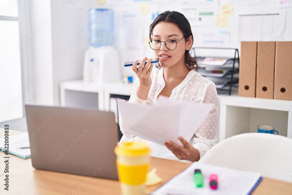 Young hispanic woman business worker talking on smartphone reading document at office Young hispanic woman business worker talking on smartphone reading document at office