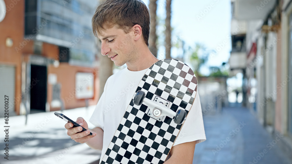 Young caucasian man using smartphone holding skate at street Young caucasian man using smartphone holding skate at street