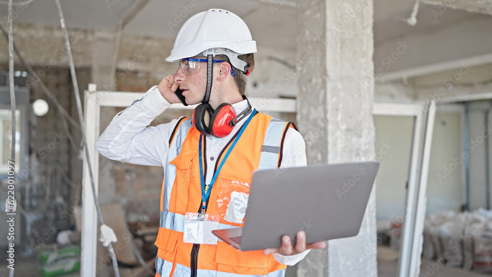 Young caucasian man architect talking on smartphone using laptop at construction site Young caucasian man architect talking on smartphone using laptop at construction site