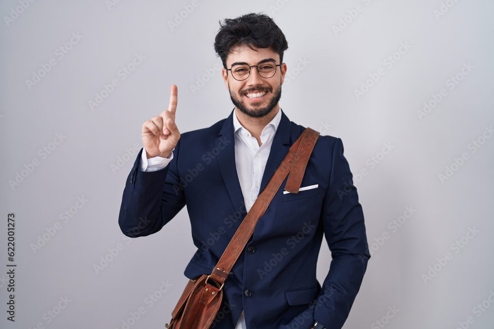 Hispanic man with beard wearing business clothes showing and pointing up with finger number one while smiling confident and happy. Hispanic man with beard wearing business clothes showing and pointing up with finger number one while smiling confident and happy.