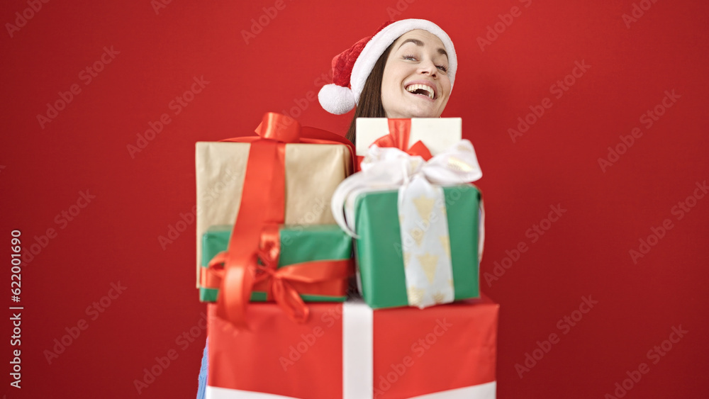 Young caucasian woman wearing christmas hat holding gifts over isolated red background