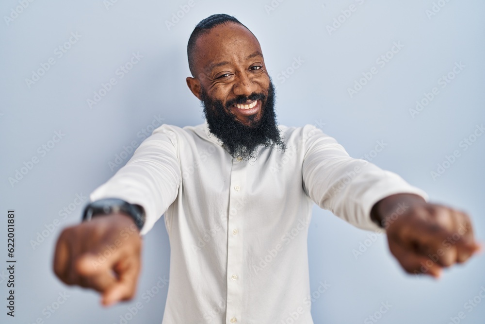 African american man standing over blue background pointing to you and the camera with fingers, smiling positive and cheerful African american man standing over blue background pointing to you and the camera with fingers, smiling positive and cheerful