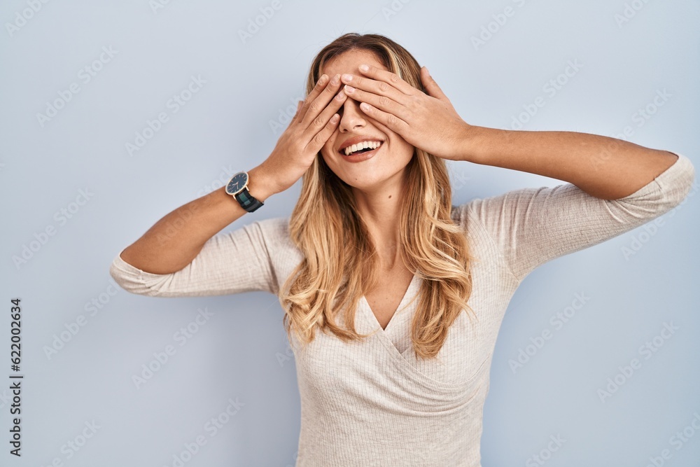 Young blonde woman standing over isolated background covering eyes with hands smiling cheerful and funny. blind concept. Young blonde woman standing over isolated background covering eyes with hands smiling cheerful and funny. blind concept.