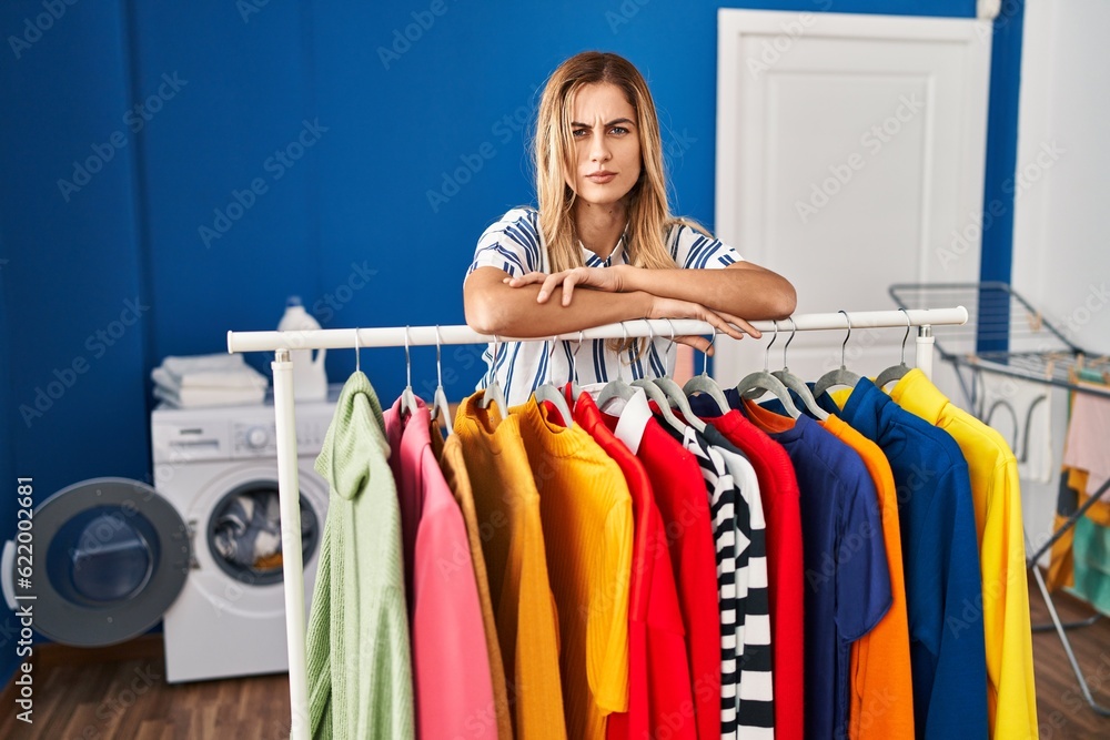 Young blonde woman at laundry room with clean clothes skeptic and nervous, frowning upset because of problem. negative person. Young blonde woman at laundry room with clean clothes skeptic and nervous, frowning upset because of problem. negative person.