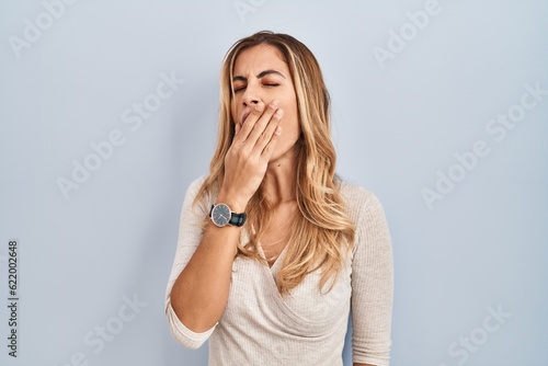 Young blonde woman standing over isolated background bored yawning tired covering mouth with hand. restless and sleepiness.