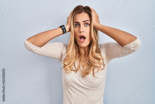 Young blonde woman standing over isolated background crazy and scared with hands on head, afraid and surprised of shock with open mouth