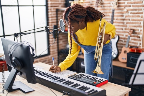 African american woman musician composing song holding trumpet at music studio