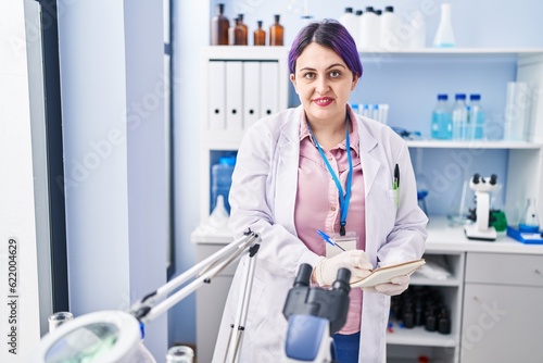 Young beautiful plus size woman scientist writing on notebook at laboratory