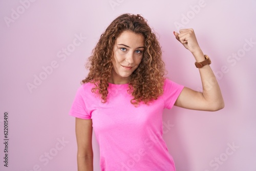 Young caucasian woman standing over pink background strong person showing arm muscle, confident and proud of power
