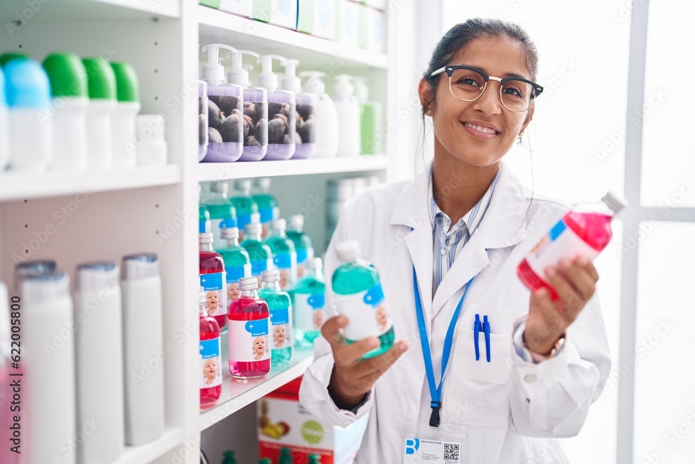 Young beautiful hispanic woman pharmacist smiling confident holding medication  bottles at pharmacy