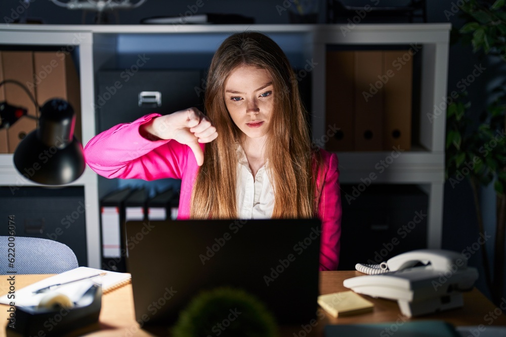Young caucasian woman working at the office at night looking unhappy and angry showing rejection and negative with thumbs down gesture. bad expression. Young caucasian woman working at the office at night looking unhappy and angry showing rejection and negative with thumbs down gesture. bad expression.