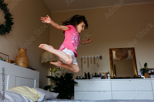 little girl in pink pajamas jumping in the parents bed