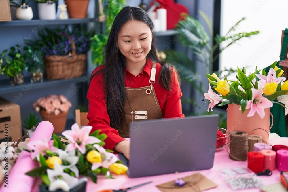 Young chinese woman florist smiling confident using laptop at flower shop