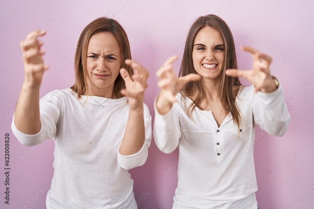 Middle age mother and young daughter standing over pink background shouting frustrated with rage, hands trying to strangle, yelling mad Middle age mother and young daughter standing over pink background shouting frustrated with rage, hands trying to strangle, yelling mad