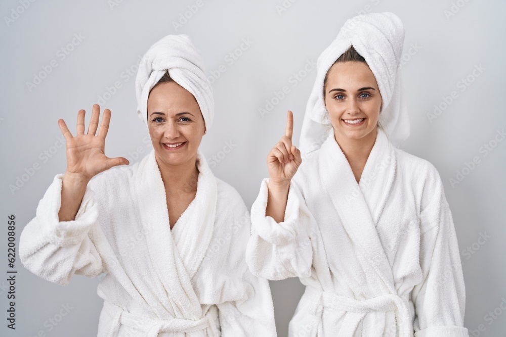 Middle age woman and daughter wearing white bathrobe and towel showing and pointing up with fingers number six while smiling confident and happy. Middle age woman and daughter wearing white bathrobe and towel showing and pointing up with fingers number six while smiling confident and happy.