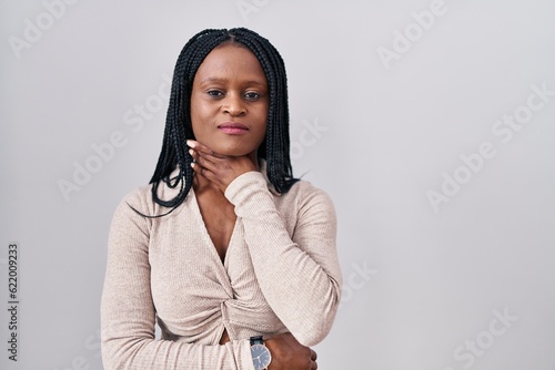 African woman with braids standing over white background touching painful neck, sore throat for flu, clod and infection