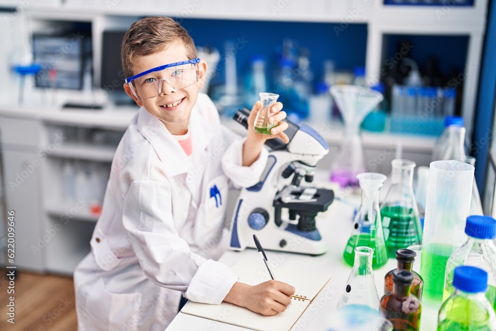 Blond child wearing scientist uniform writing on notebook at laboratory Blond child wearing scientist uniform writing on notebook at laboratory