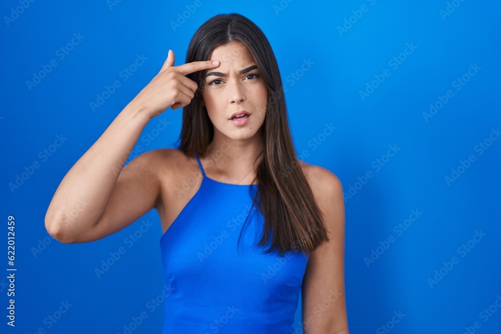 Hispanic woman standing over blue background pointing unhappy to pimple on forehead, ugly infection of blackhead. acne and skin problem Hispanic woman standing over blue background pointing unhappy to pimple on forehead, ugly infection of blackhead. acne and skin problem