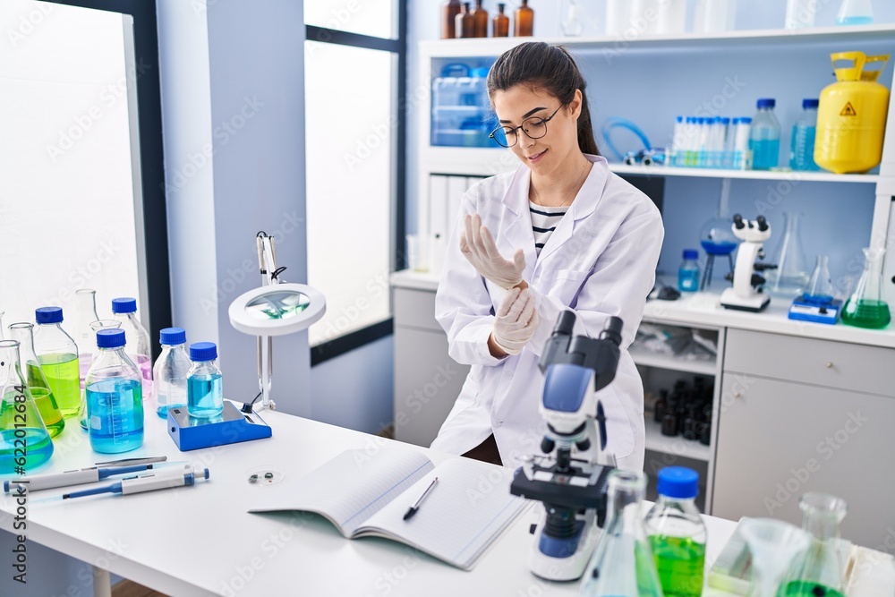 Young beautiful hispanic woman scientist smiling confident wearing gloves at laboratory
