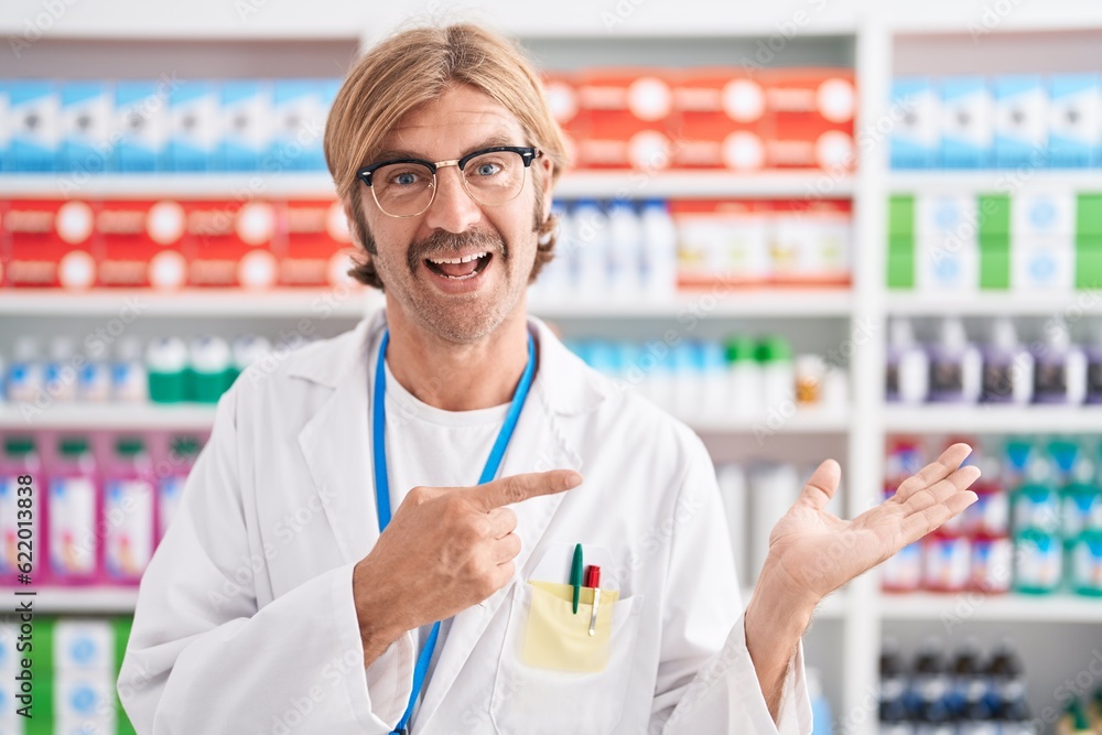 Caucasian man with mustache working at pharmacy drugstore amazed and smiling to the camera while presenting with hand and pointing with finger. Caucasian man with mustache working at pharmacy drugstore amazed and smiling to the camera while presenting with hand and pointing with finger.