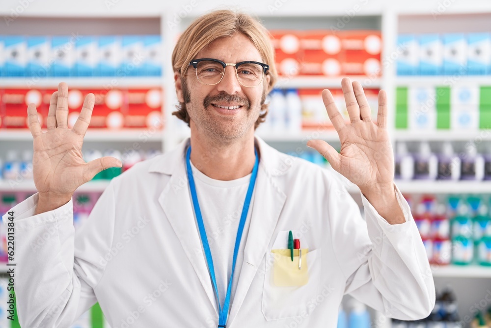 Caucasian man with mustache working at pharmacy drugstore showing and pointing up with fingers number ten while smiling confident and happy. Caucasian man with mustache working at pharmacy drugstore showing and pointing up with fingers number ten while smiling confident and happy.
