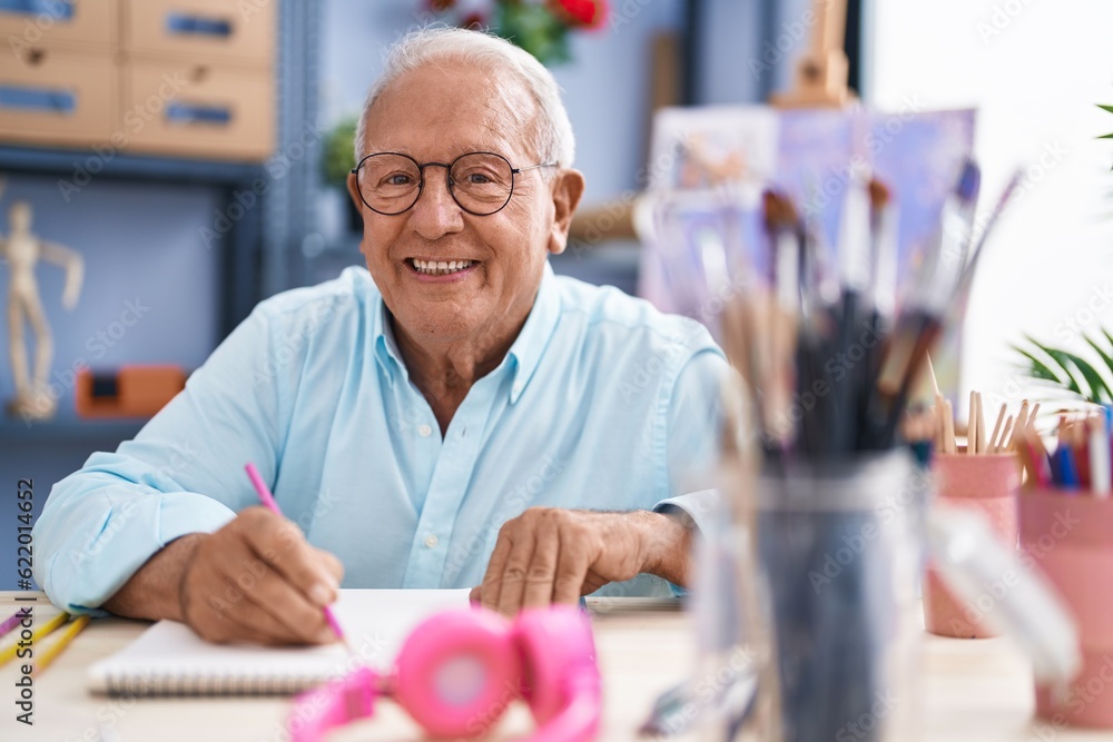 Senior grey-haired man artist smiling confident drawing on notebook at art studio Senior grey-haired man artist smiling confident drawing on notebook at art studio