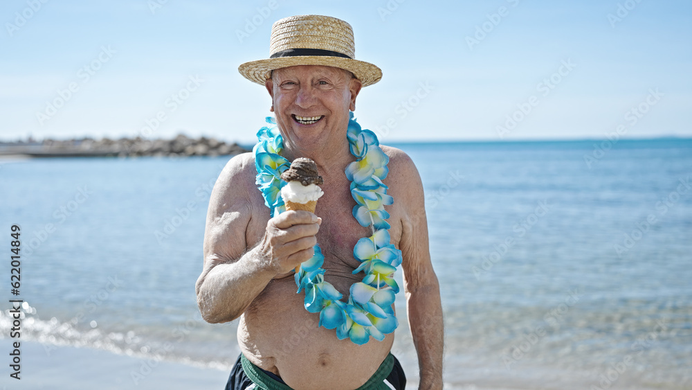 Senior grey-haired man tourist wearing swimsuit and summer hat holding ice cream at seaside