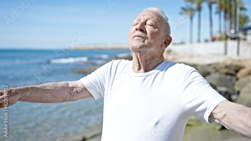 Senior grey-haired man breathing with closed eyes at seaside