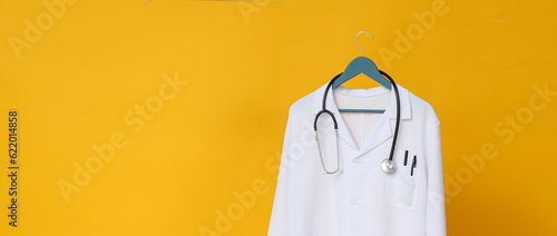 White coat of a doctor with a stethoscope on a yellow background, place for text