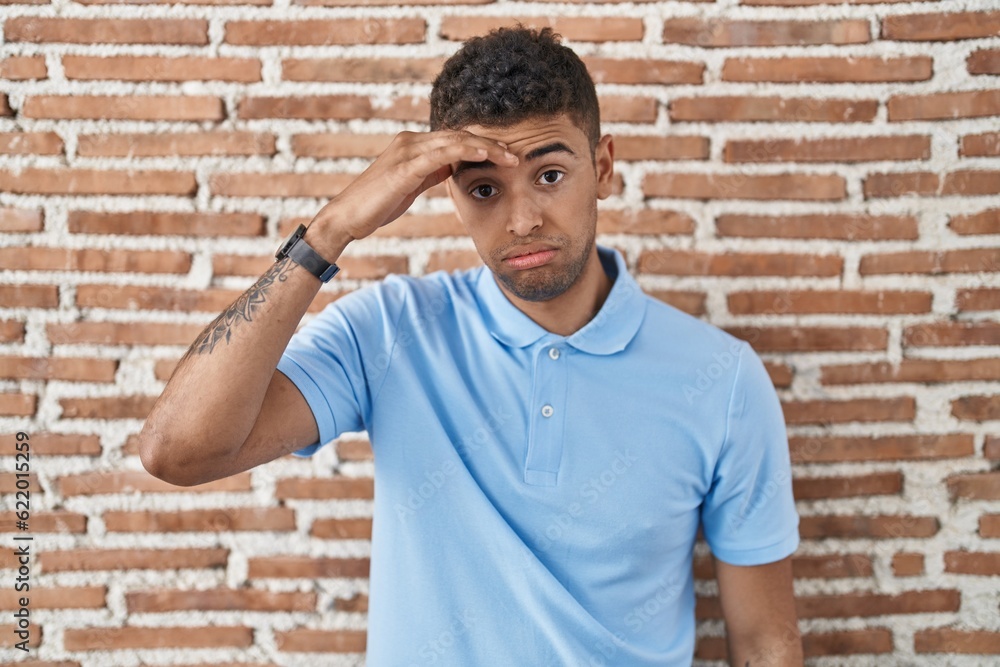 Brazilian young man standing over brick wall worried and stressed about a problem with hand on forehead, nervous and anxious for crisis Brazilian young man standing over brick wall worried and stressed about a problem with hand on forehead, nervous and anxious for crisis