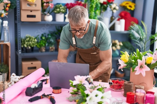 Middle age grey-haired man florist using laptop standing at flower shop