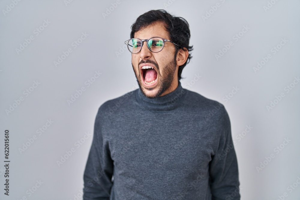 Handsome latin man standing over isolated background angry and mad screaming frustrated and furious, shouting with anger. rage and aggressive concept.