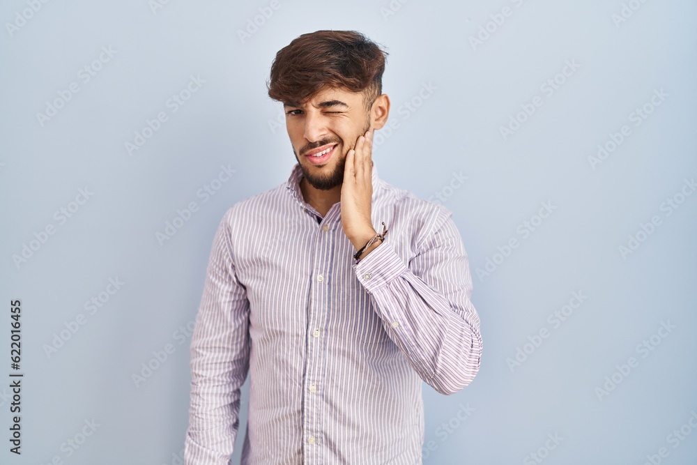 Arab man with beard standing over blue background touching mouth with hand with painful expression because of toothache or dental illness on teeth. dentist Arab man with beard standing over blue background touching mouth with hand with painful expression because of toothache or dental illness on teeth. dentist