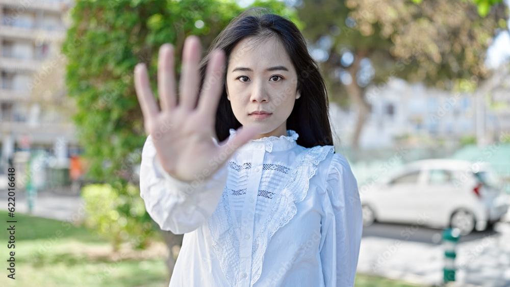 Young chinese woman doing stop gesture with hand at park