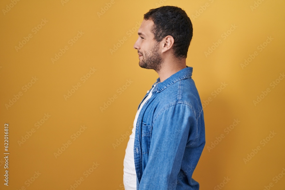Hispanic man standing over yellow background looking to side, relax profile pose with natural face and confident smile. Hispanic man standing over yellow background looking to side, relax profile pose with natural face and confident smile.