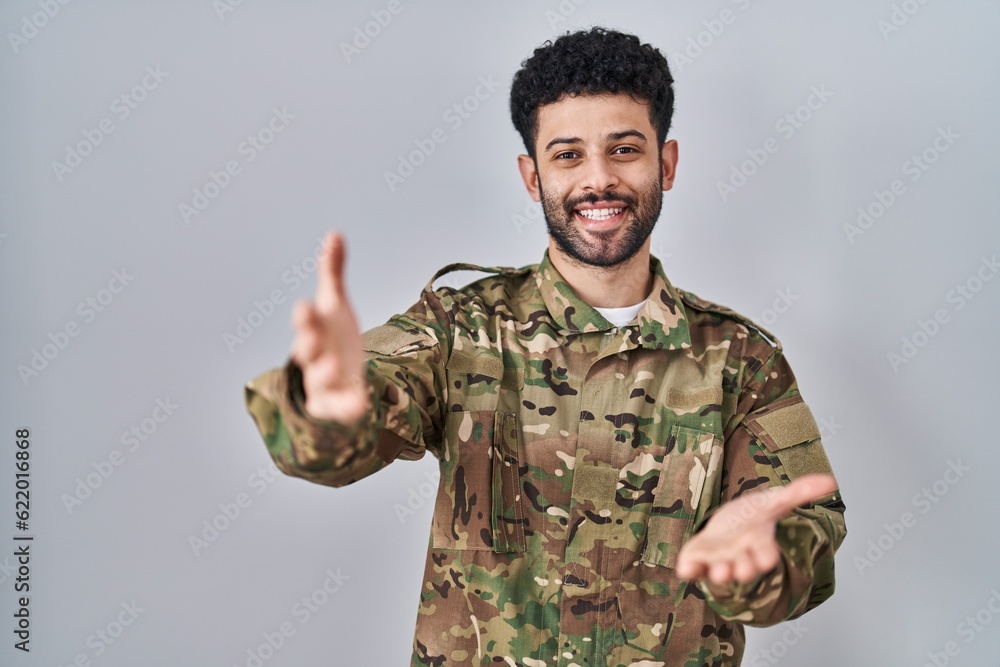 Arab man wearing camouflage army uniform smiling cheerful offering hands giving assistance and acceptance.