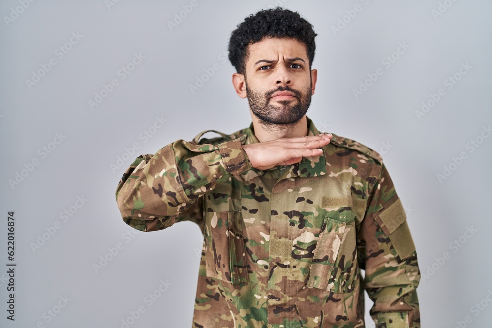 Arab man wearing camouflage army uniform cutting throat with hand as knife, threaten aggression with furious violence