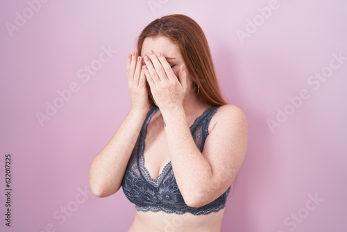 Redhead woman wearing lingerie over pink background with sad expression covering face with hands while crying. depression concept. © Krakenimages.com