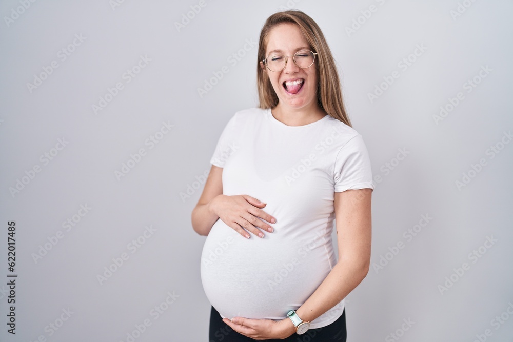 Young pregnant woman expecting a baby, touching pregnant belly sticking tongue out happy with funny expression. Young pregnant woman expecting a baby, touching pregnant belly sticking tongue out happy with funny expression.