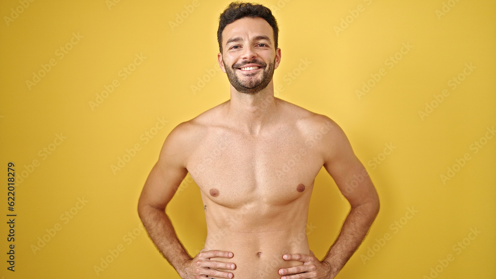 Young hispanic man tourist smiling confident standing shirtless over isolated yellow background