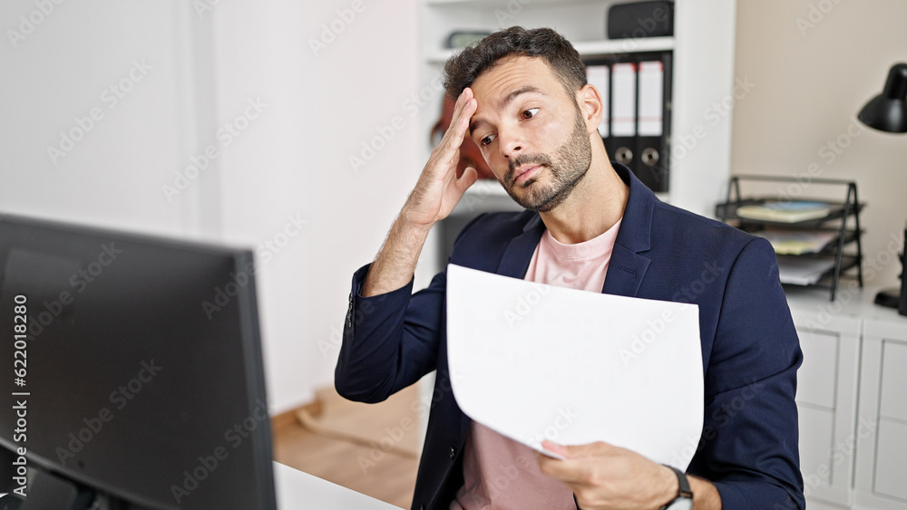 Young hispanic man business worker using computer reading document stressed at office Young hispanic man business worker using computer reading document stressed at office