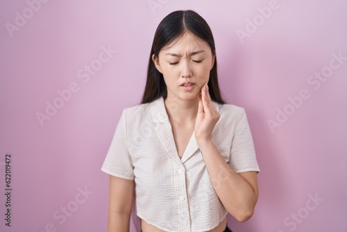 Chinese young woman standing over pink background touching mouth with hand with painful expression because of toothache or dental illness on teeth. dentist © Krakenimages.com