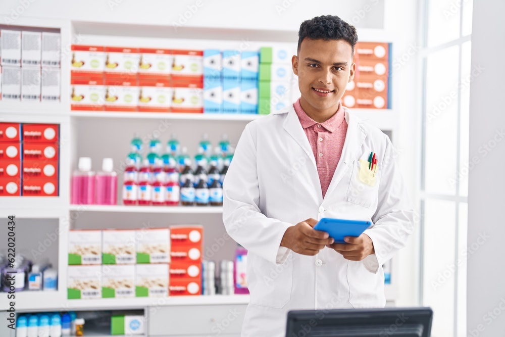 Young latin man pharmacist smiling confident using touchpad at pharmacy